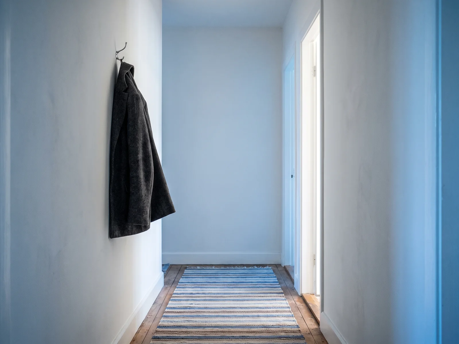 A quiet hallway in morning light with a coat on a hook and a striped runner.